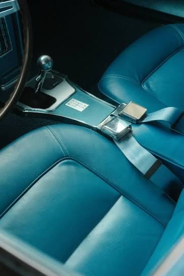 A vintage blue vehicle interior with a lap seatbelt fastened across the seat