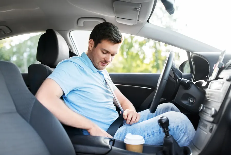 A driver in a blue shirt seated in a car, fastening the seatbelt across the chest