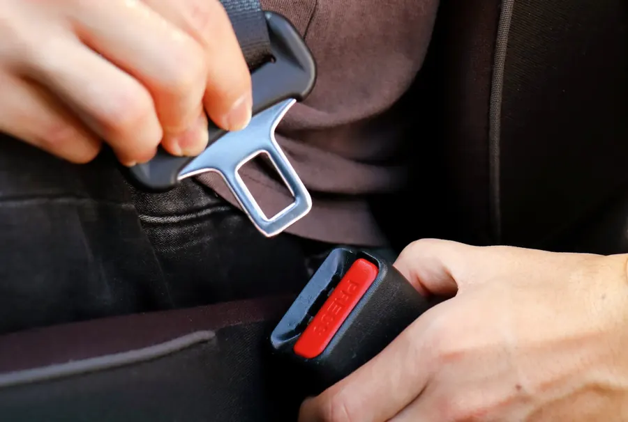 Two hands guiding a seatbelt tongue into a black buckle with a red release button