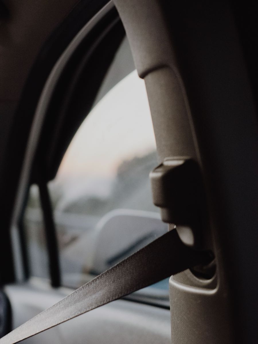 A seatbelt running past a vehicle door pillar with soft daylight through the window