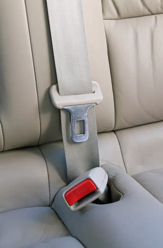 A grey three-point seatbelt running over a light vehicle seat with its tongue and buckle visible